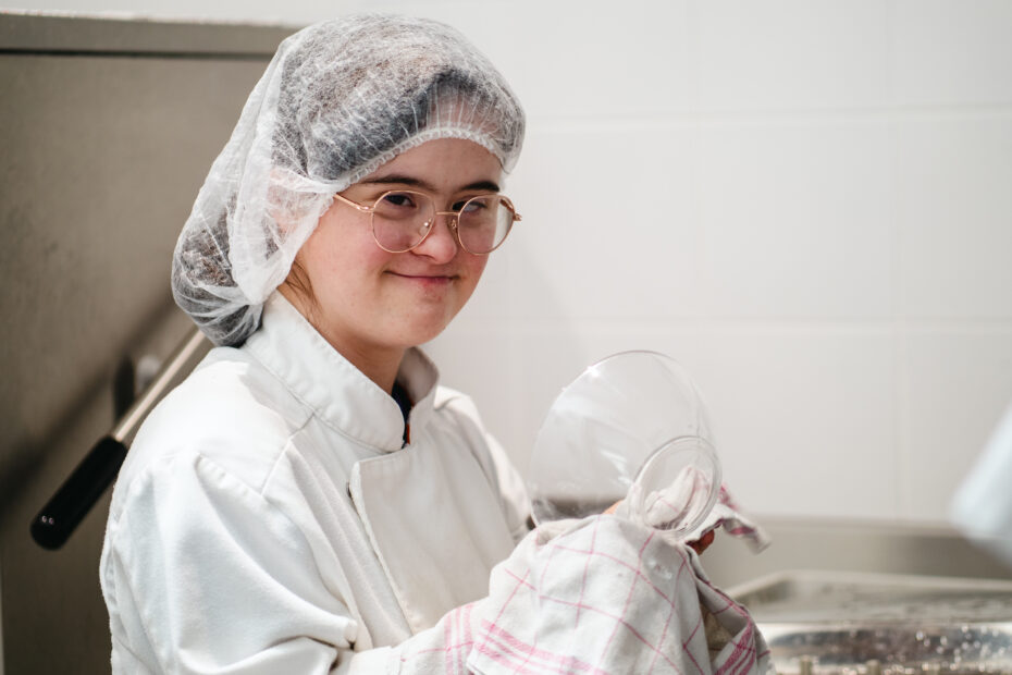 L'image montre une jeune femme avec déficience intellectuelle entrain de travailler dans un restaurant.